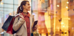 A woman with shopping bags looking in a store window holding a phone
