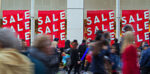 a busy high street with shoppers walking past a store with for sale signs on show