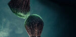 two makeup brushes against a dark background